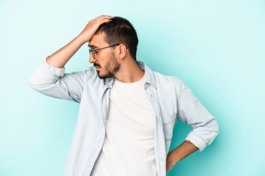 Kafkasyalı genç adam mavi arka planda izole edilmiş bir şekilde bir şeyi unutuyor. Alnına avuç içi ve gözlerini kapayarak vuruyor..