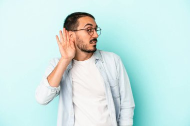 Mavi arka planda izole edilmiş genç beyaz adam bir dedikoduyu dinlemeye çalışıyor..