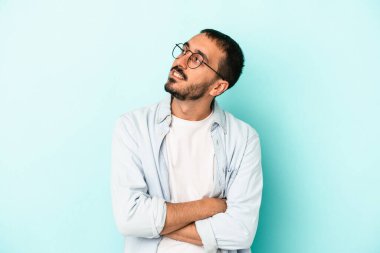 Kafkasyalı genç adam mavi arka planda izole edilmiş hedeflerine ve amaçlarına ulaşma hayali kuruyor.