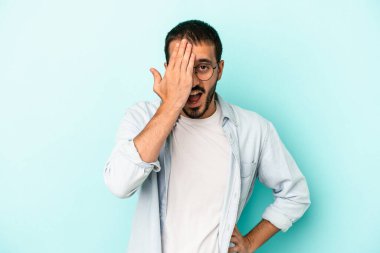 Mavi arka planda izole edilmiş genç beyaz adam yüzünün yarısını palmiye ile kaplayarak eğleniyor..