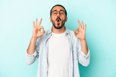 Mavi arka planda izole edilmiş genç beyaz adam yorucu bir günün ardından rahatlıyor. Yoga yapıyor..