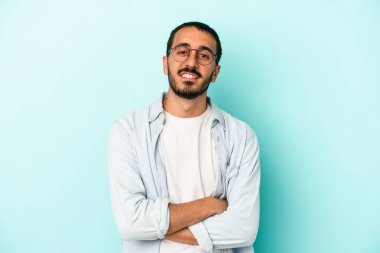 Mavi arka planda kendini güvende hisseden, kararlılıkla kollarını kavuşturan genç beyaz bir adam..