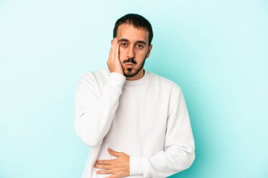 Mavi arka planda izole edilmiş genç beyaz adamın yanakları şişer, yorgun bir ifadesi vardır. Yüz ifadesi kavramı.