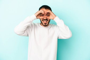 Mavi arka planda izole edilmiş genç beyaz adam gözlerinde sorun olmadığını gösteriyor.