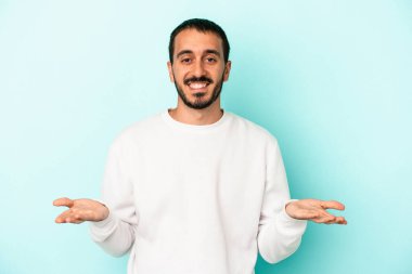 Mavi arka planda izole genç beyaz adam kollarıyla ölçek yapar, mutlu ve kendinden emin hisseder..