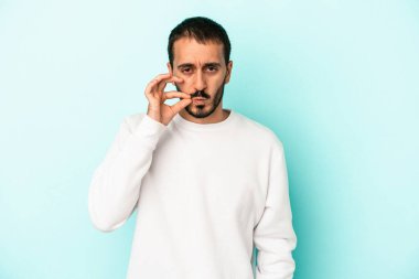 Genç beyaz adam mavi arka planda izole edilmiş ve parmakları dudaklarında bir sır saklıyor..