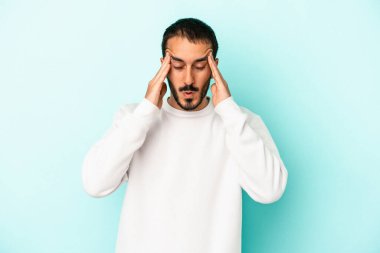 Kafkasyalı genç bir adam mavi arka planda izole edilmiş, başı ağrıyor, yüzüne dokunuyor..