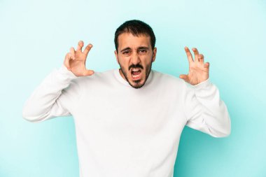 Mavi arka planda izole edilmiş genç beyaz adam pençelerini kedi taklidi yaparken gösteriyor, agresif bir hareket..