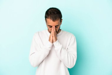 Kafkasyalı genç adam mavi arka planda izole edilmiş dua ediyor, bağlılık gösteriyor, dindar biri ilahi ilham arıyor..