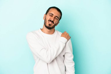 Mavi arka planda izole edilmiş, omuz ağrısı olan genç beyaz bir adam..
