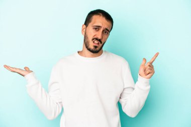 Kafkasyalı genç adam mavi arka planda izole edilmiş ve elinde bir ürün tutuyor..