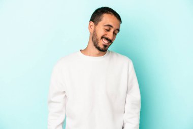 Mavi arka planda izole edilmiş genç beyaz adam gülüyor ve gözlerini kapıyor, rahatlamış ve mutlu hissediyor..