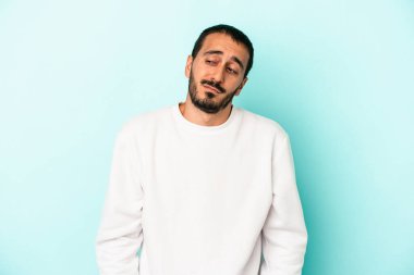 Mavi arka planda izole edilmiş genç beyaz adam omuzlarını silkeliyor ve gözleri açık..