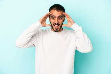 Mavi arka planda izole edilmiş genç beyaz adam hoş bir sürpriz alıyor, heyecanlı ve el kaldırıyor..