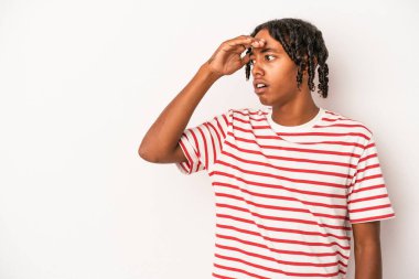 Genç Afrikalı Amerikalı adam beyaz arka planda izole edilmiş, uzaklara bakıyor ve elini alnına koyuyor..