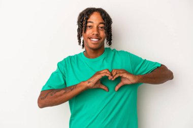 Beyaz arka planda izole edilmiş genç Afrikalı Amerikalı adam gülümsüyor ve elleriyle kalp şekli gösteriyor..