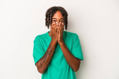 Genç Afro-Amerikalı bir adam beyaz arka planda izole edilmiş bir şekilde bir şeylere gülüyor, elleriyle ağzını kapatıyor..