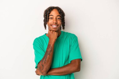 Beyaz arka planda izole edilmiş, mutlu ve kendinden emin gülümseyen, elleriyle çenesine dokunan genç bir Afrikalı Amerikalı..