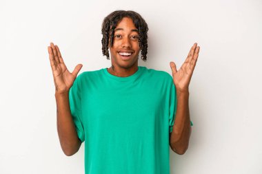 Genç Afrikalı Amerikalı bir adam beyaz arka planda izole edilmiş zaferi ya da başarıyı kutluyor, şaşırmış ve şok olmuş..