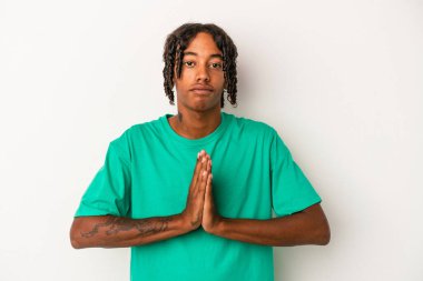Genç Afrikalı Amerikalı adam beyaz arka planda izole edilmiş dua ediyor, bağlılık gösteriyor, dindar biri ilahi ilham arıyor..