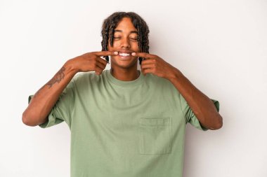 Beyaz arka planda izole edilmiş genç Afrikalı Amerikalı adam gülümsüyor, parmaklarını ağıza doğrultuyor..