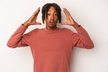 Genç Afrikalı Amerikalı bir adam beyaz arka planda izole edilmiş zaferi ya da başarıyı kutluyor, şaşırmış ve şok olmuş..