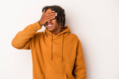 Beyaz arka planda izole edilmiş genç Afro-Amerikan erkeği elleriyle gözlerini kapatıyor, gülümseyerek bir sürpriz bekliyor..