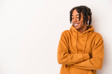 Beyaz arka planda izole edilmiş genç Afro-Amerikalı adam kollarını kavuşturarak gülümsüyor..