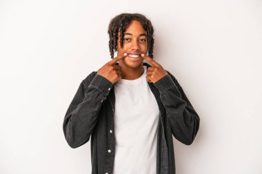 Beyaz arka planda izole edilmiş genç Afrikalı Amerikalı adam gülümsüyor, parmaklarını ağıza doğrultuyor..