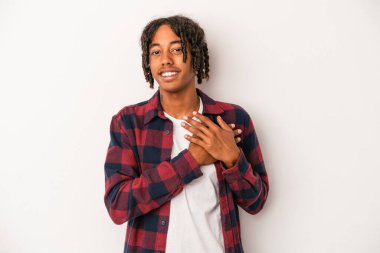 Genç Afrikalı Amerikalı adam beyaz arka planda soyutlanmış gülüyor, ellerini yüreğine koyuyor, mutluluk kavramını koruyor..