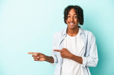 Genç Afro-Amerikalı adam mavi arka planda izole edilmiş. İşaret parmaklarıyla işaret ederek heyecanlı..