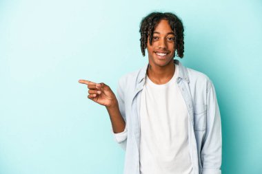 Genç Afrikalı Amerikalı adam mavi arka planda izole edilmiş, mutlu bir şekilde işaret parmağıyla işaret ederek gülümsüyor..