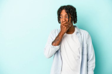 Genç Afrikalı Amerikalı bir adam mavi arka planda izole edilmiş. Düşünceli bir şekilde bir fotokopi odasına bakıyor. Ağzını eliyle kapatıyor..