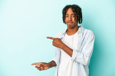 Mavi arka planda izole edilmiş genç Afro-Amerikalı adam işaret parmağıyla fotokopi alanını işaret ederek şok oldu..