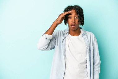 Genç Afro-Amerikalı adam mavi arka planda izole edilmiş yüksek sesle bağırıyor, gözlerini açık ve ellerini gergin tutuyor.