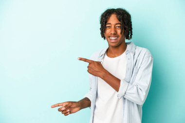 Genç Afrikalı Amerikalı bir adam mavi arka planda izole edilmiş ve işaret parmaklarıyla fotokopi alanını işaret ederek heyecan ve arzusunu ifade ediyor..