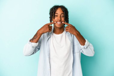 Genç Afrikalı Amerikalı adam mavi arka planda izole edilmiş gülümsüyor, parmaklarını ağıza doğrultuyor..