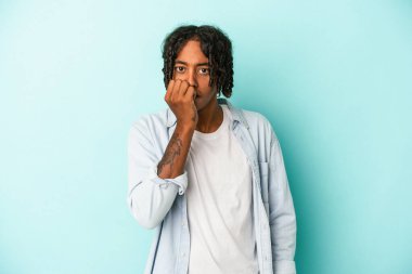 Genç Afrikalı Amerikalı bir adam mavi arka planda izole edilmiş tırnak yiyor, gergin ve çok endişeli..
