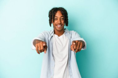 Genç Afro-Amerikalı adam mavi arka planda izole edildi. Neşeli gülümsemeler ön tarafı işaret ediyor..
