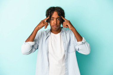 Genç Afrikalı Amerikalı bir adam mavi arka planda izole edilmiş vazifesine odaklanmış, işaret parmaklarını işaret ediyor..