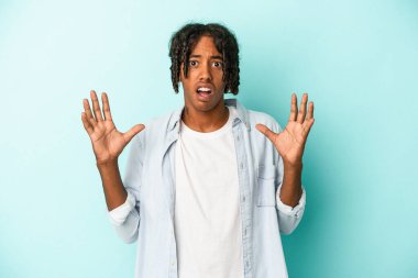 Genç Afrikalı Amerikalı adam mavi arka planda izole edilmiş gökyüzüne haykırıyor, yukarı bakıyor, hayal kırıklığına uğramış..