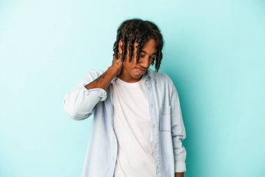 Genç Afrikalı Amerikalı bir adam mavi arka planda izole edilmiş. Oturaklı yaşam tarzından dolayı boyun ağrısı çekiyor..