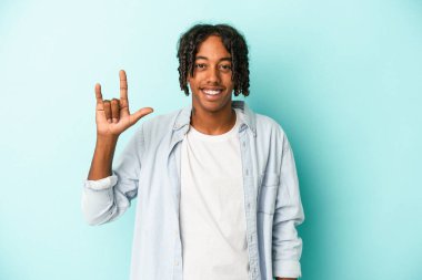 Genç Afrikalı Amerikalı bir adam mavi arka planda izole edilmiş bir şekilde boynuz hareketi bir devrim konsepti olarak gösteriyor..