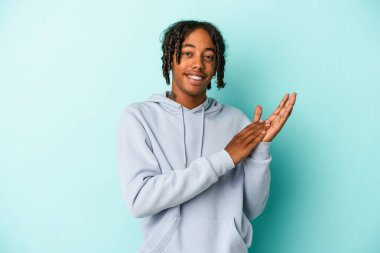 Genç Afrikalı Amerikalı erkek mavi arka planda izole edilmiş enerjik ve rahat hissediyor, kendinden emin ellerini ovuşturuyor..