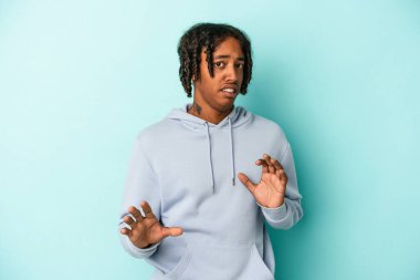 Genç Afrikalı Amerikalı bir adam mavi arka planda izole edilmiş, tiksinti belirtisi gösteren birini reddediyor..