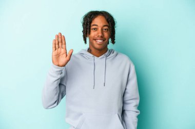 Genç Afro-Amerikalı adam mavi arka planda izole edilmiş. Gülümsüyor. Beş numarayı parmaklarıyla gösteriyor..