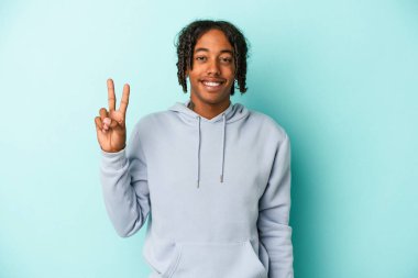 Genç Afrikalı Amerikalı adam mavi arka planda izole edilmiş neşeli ve kaygısız parmakları olan bir barış sembolü gösteriyor..