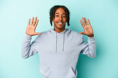 Mavi arka planda izole edilmiş genç Afro-Amerikalı adam on numarayı elleriyle gösteriyor..