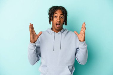 Genç Afro-Amerikan erkeği mavi arka planda izole edilmiş bir şekilde zaferi ya da başarıyı kutluyor. Şaşırmış ve şok olmuş..