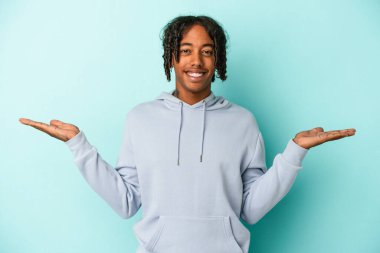 Mavi arka planda izole edilmiş genç Afrikalı Amerikalı adam kollarıyla ölçek oluşturuyor, mutlu ve kendinden emin hissediyor..